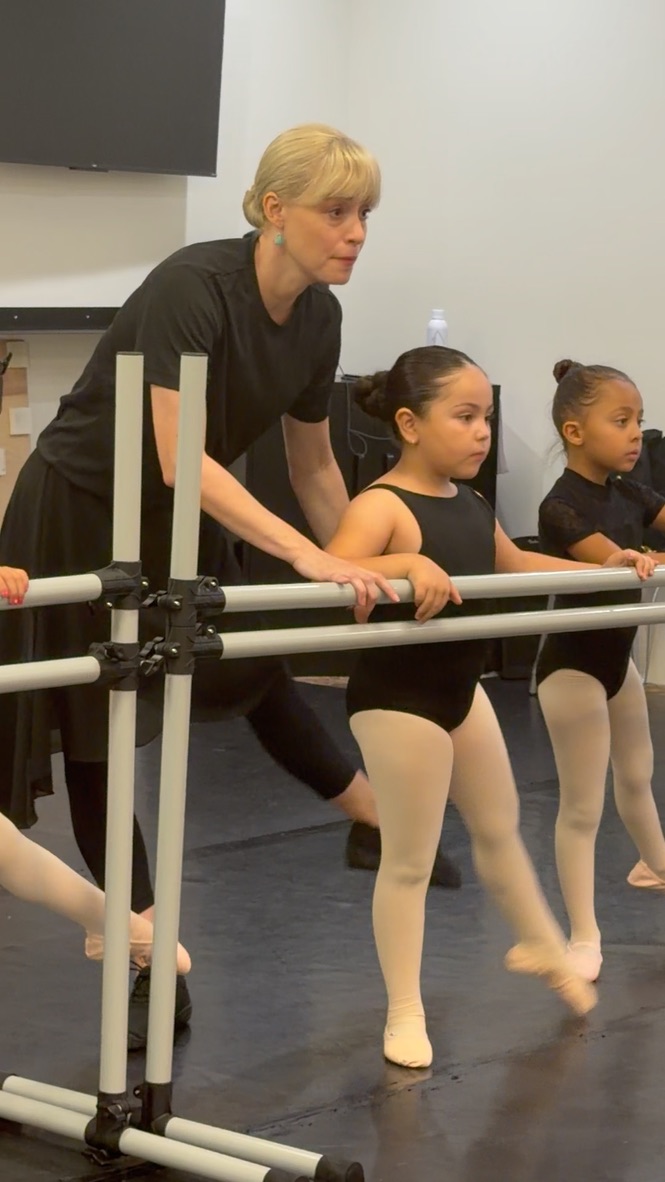 A ballet teacher guiding young dancers at the barre