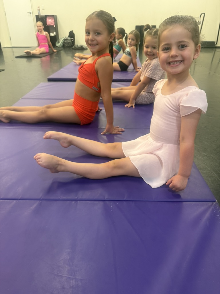 Young dancers smiling while seated on purple mats during class